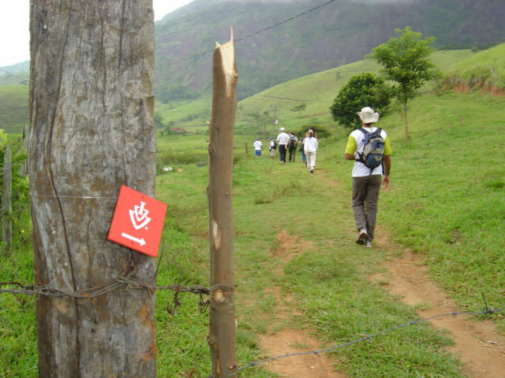 Peregrinos caminhando em área rural com sinalização do IVV